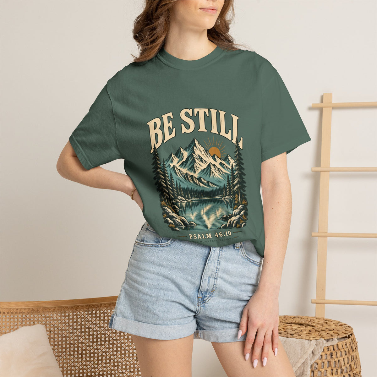 Female model wearing the Blue Spruce Be Still Christian mountain T-shirt with denim shorts.